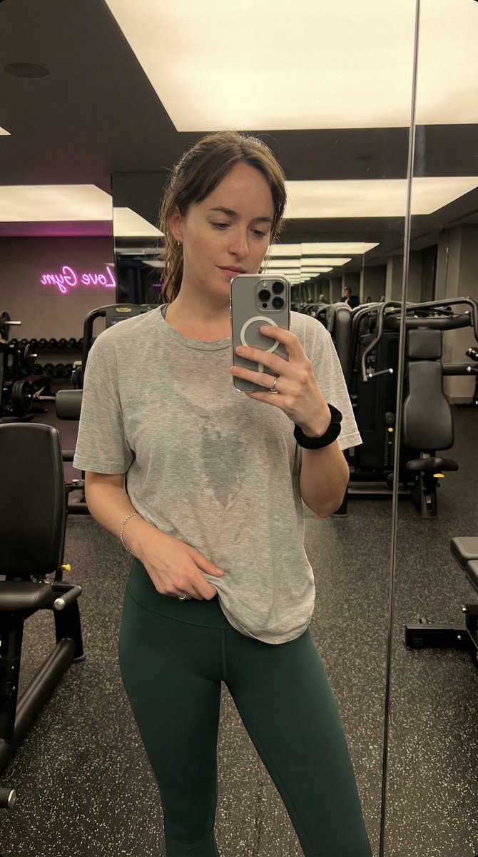 现代健身房内 Madelyn Cline 的写实风格、高度精细的抓拍式智能手机镜面自拍。她拥有运动型、曲线优美且健美的身材，腰部线条分明。她穿着一件薄的、宽松的浅蓝色短袖 T 恤…