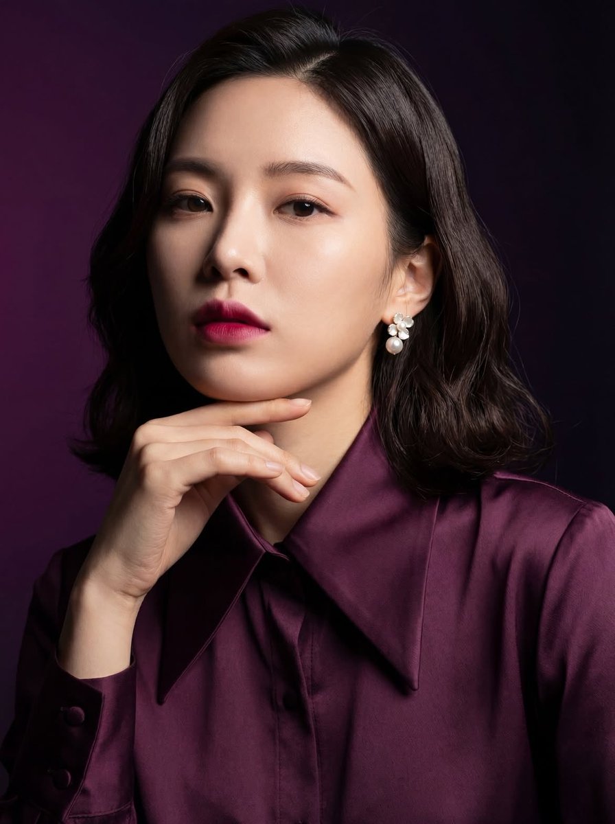 "一张优雅东亚女性的影棚肖像，肩长的深色头发，身着深梅紫色缎面衬衫，柔和自然的妆容搭配大胆的粉色唇彩，佩戴珍珠花卉耳环，手轻托下巴，神情自信而沉静，皮肤光滑无瑕，戏剧化的柔和光线…