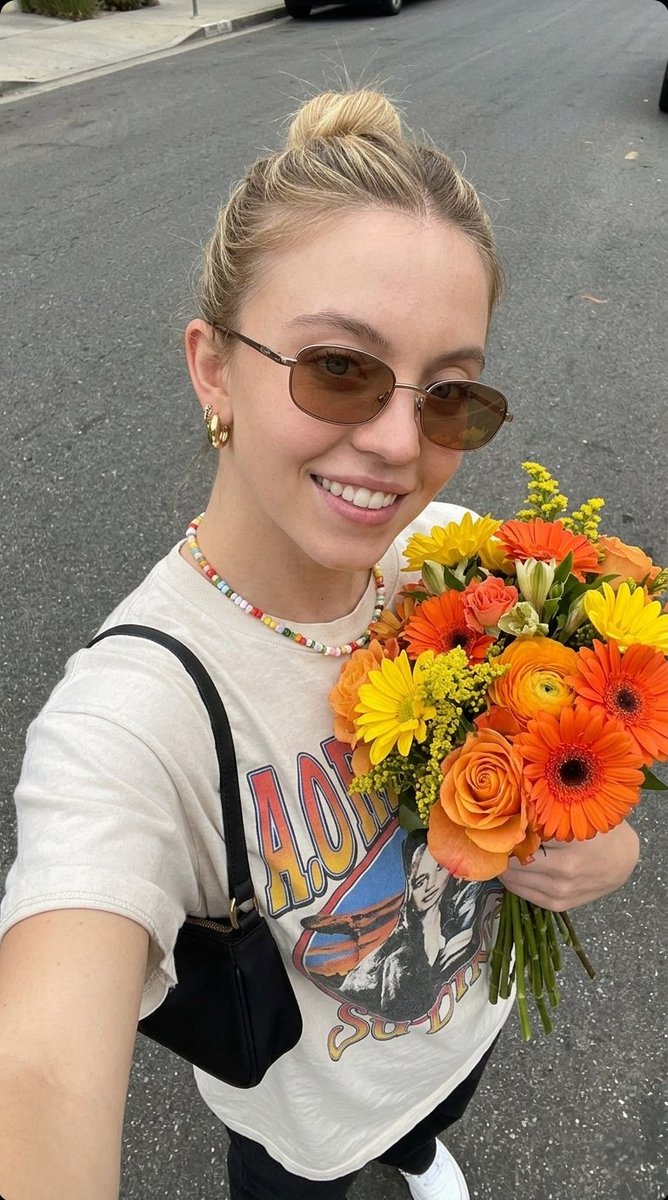 超现实自拍照片，一位年轻女子手持一束新鲜花束， 姿势：俯拍自拍角度，将花束贴近胸前，浅浅微笑，自然放松的表情， 外观：肌肤洁净有光泽，头发整齐地盘成发髻，柔和自然妆容，唇部水润亮…