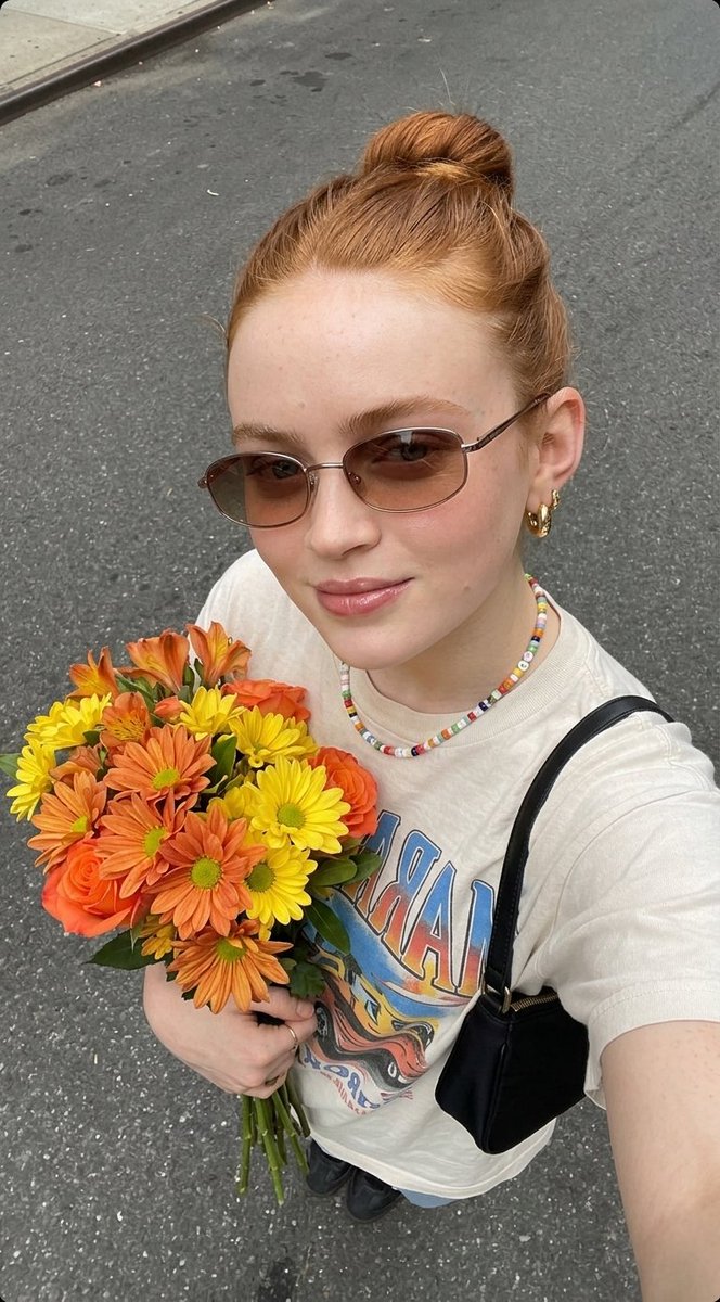 超现实自拍照片，一位年轻女子手持一束新鲜花束， 姿势：俯拍自拍角度，将花束贴近胸前，浅浅微笑，自然放松的表情， 外观：肌肤洁净有光泽，头发整齐地盘成发髻，柔和自然妆容，唇部水润亮…
