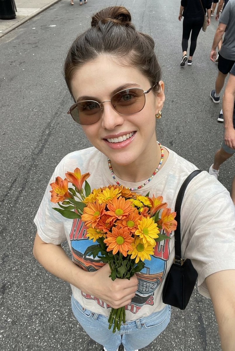 超现实自拍照片，一位年轻女子手持一束新鲜花束， 姿势：俯拍自拍角度，将花束贴近胸前，浅浅微笑，自然放松的表情， 外观：肌肤洁净有光泽，头发整齐地盘成发髻，柔和自然妆容，唇部水润亮…