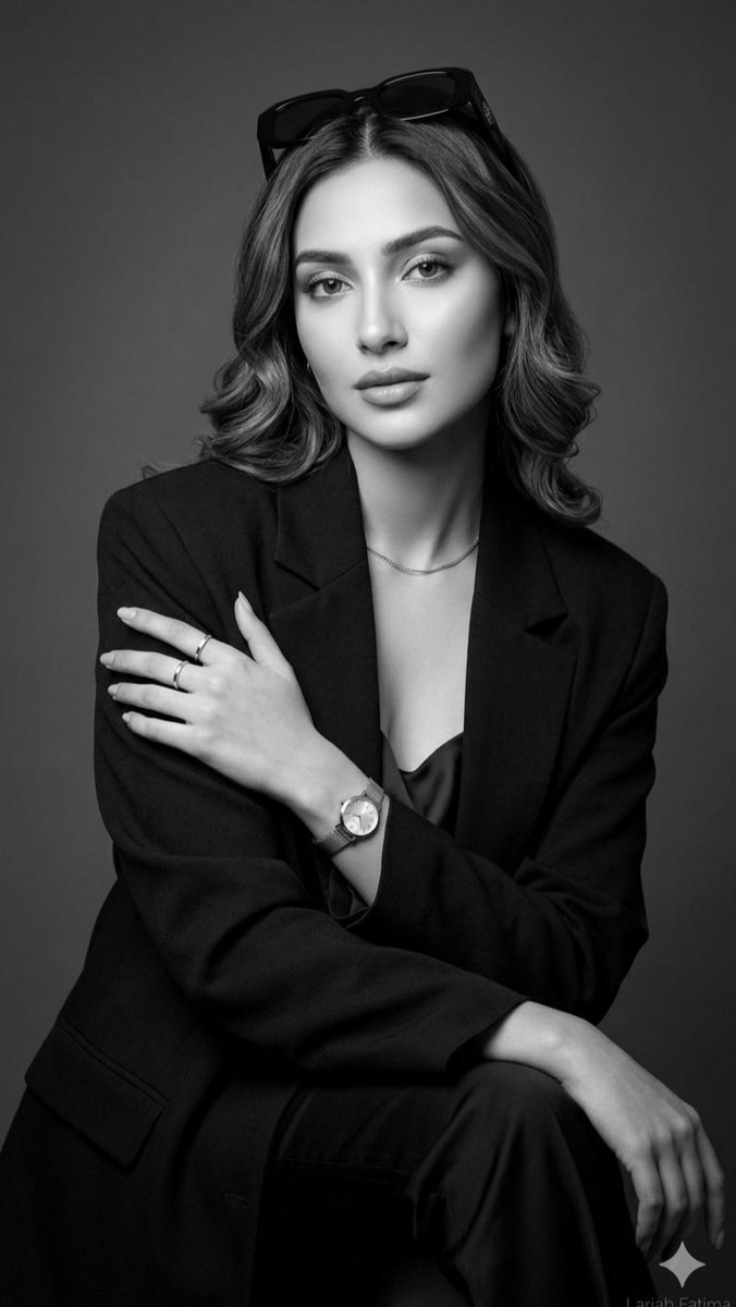 一张精致的黑白摄影棚人像照,画面中是一位举止从容优雅的年轻女性。她身穿剪裁考究的黑色西装外套,内搭丝绸吊带背心,头顶时尚地架着一副深色太阳镜。她柔软蓬松的头发被梳理成波浪卷。她佩…