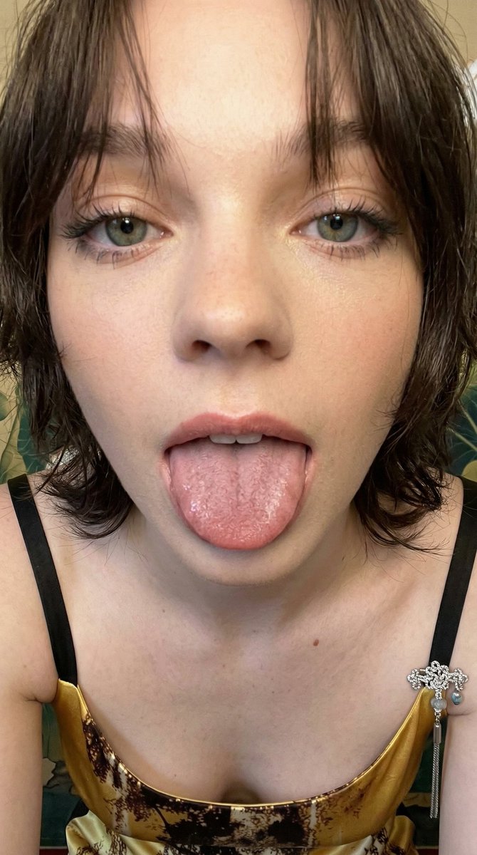 一张极近距离的智能手机业余特写肖像,捕捉到一位年轻女性面部的下半部分,她顽皮地将舌头伸向镜头。主体伸出舌头,展现出宽阔平坦的肌肉表面,布满细密的丝状乳头,并带有微微的湿润光泽。她…