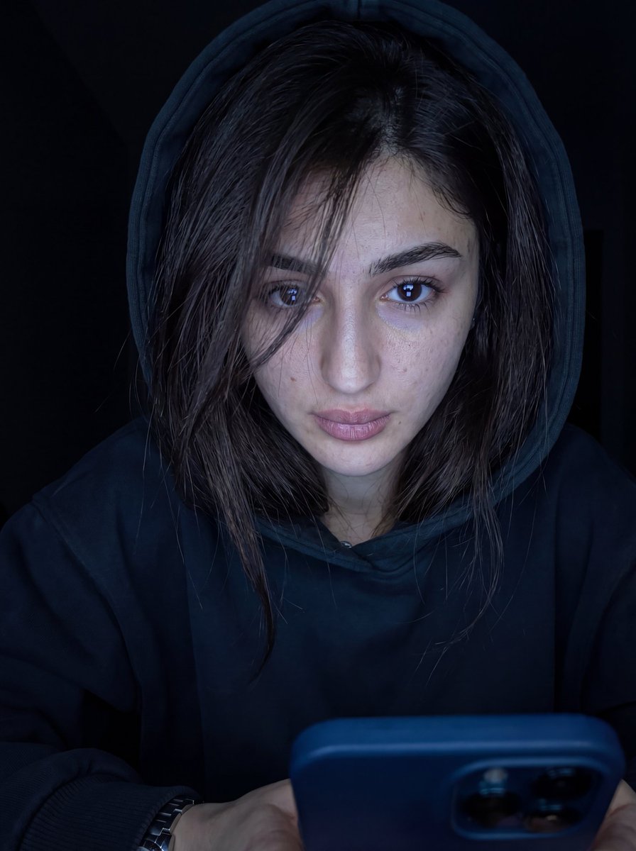 超写实特写肖像，画中人物为男性或女性（来自上传图像），凌乱的头发部分遮住一只眼睛，身穿深色 oversized 帽衫，帽子微微拉起。脸部由下方冷色调的手机屏幕光照亮，眼睛锐利地反…