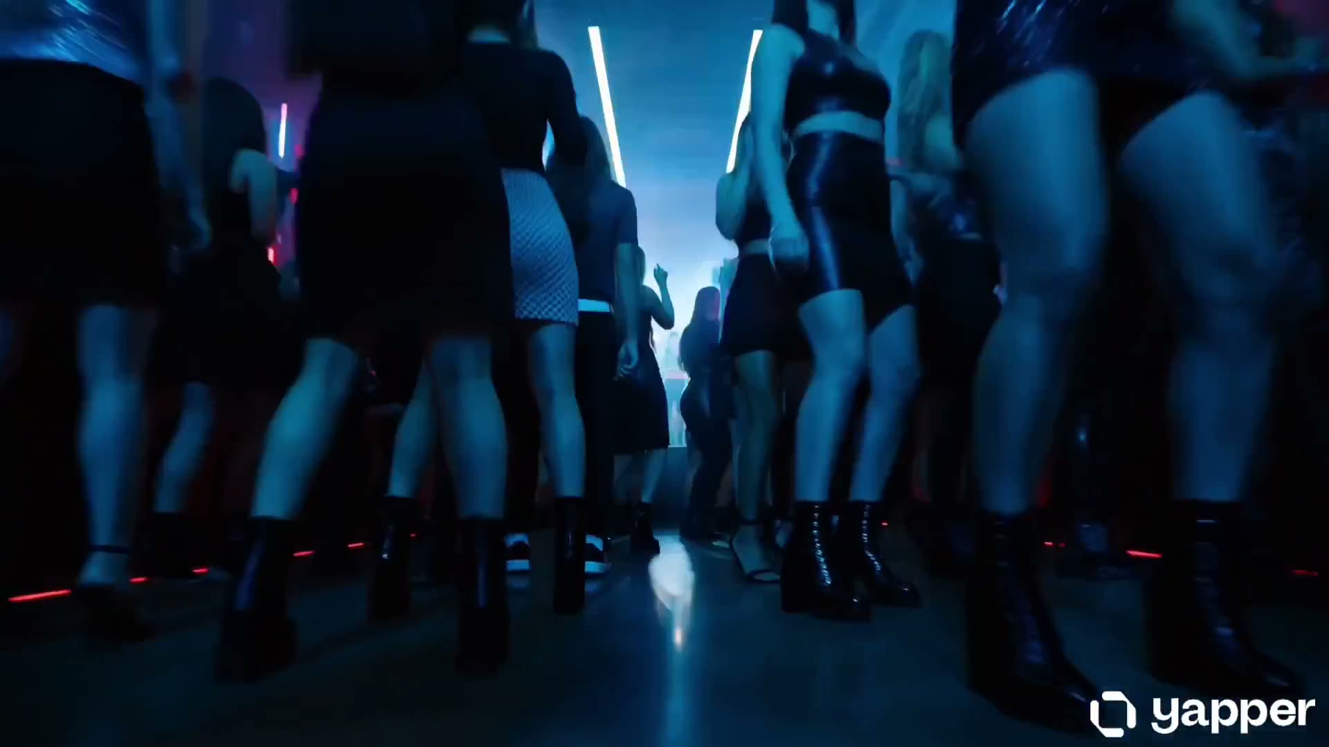 拥挤的夜店内，灯光闪烁，低音强劲。镜头穿梭于跳舞的人群之间，随后锁定主要表演者。她在一座小舞台上自信、大胆地舞动身姿。霓虹灯光闪烁不定，人群随之反应，快速剪辑…