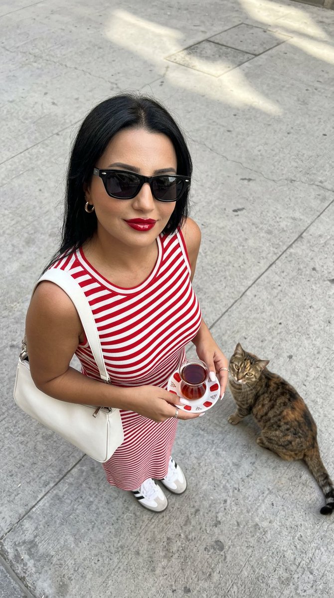 一张高角度俯视的超写实时尚摄影照片：一位时尚年轻女性站立在干净浅灰色的水泥街道上，自信而有魅力地抬头直视镜头。她留着没有头巾的深色长发，唇色为光泽的樱桃红，拥有温暖的古铜色肌肤…
