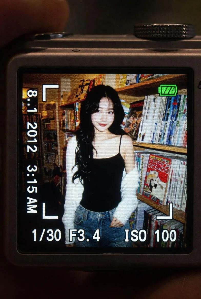 一段真实感的特写镜头:在黑暗的室内环境中,一台小型数码相机屏幕明亮地发光。LCD 屏幕上显示着一张 2010 年代早期风格的抓拍照片,照片中是一位年轻的东亚女性,留着长长的深色波…