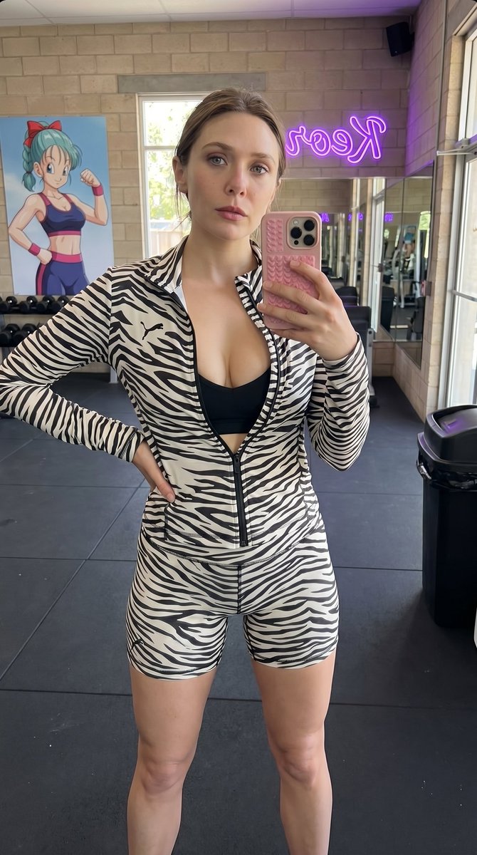 Elizabeth olsen（伊丽莎白·奥尔森）正在健身房或健身工作室里对着镜子自拍。 她的外貌与穿着： • 她身穿一套斑纹图案的运动服：长袖拉链外套，深 V 领（完全拉开，露…