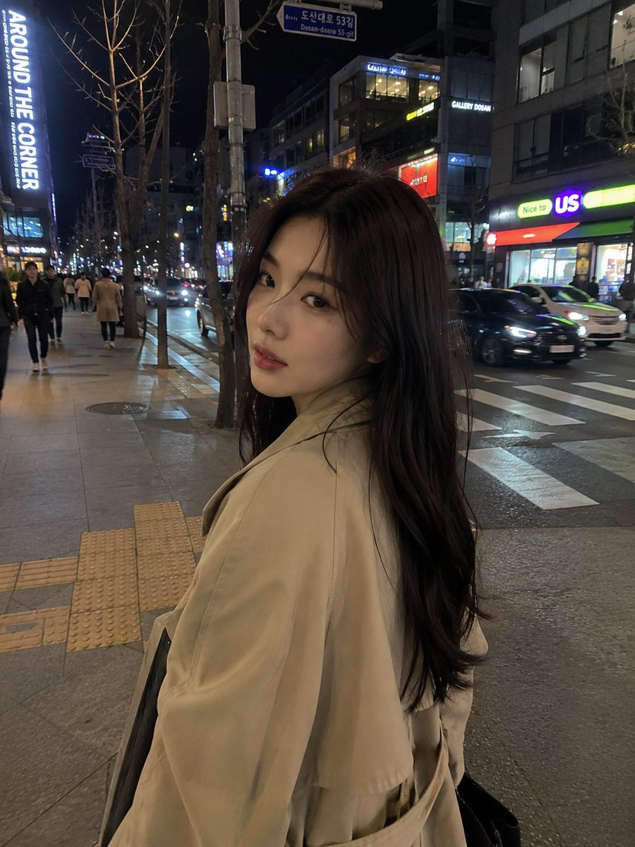 超写实的随拍 iPhone 街头照片:一位美丽的年轻韩国女孩,夜晚穿过霓虹灯闪烁的首尔街道,从侧视角抓拍,电影感的都市氛围,自然的行走姿态,黑色长发随风飘动,身穿米色超大号风衣…