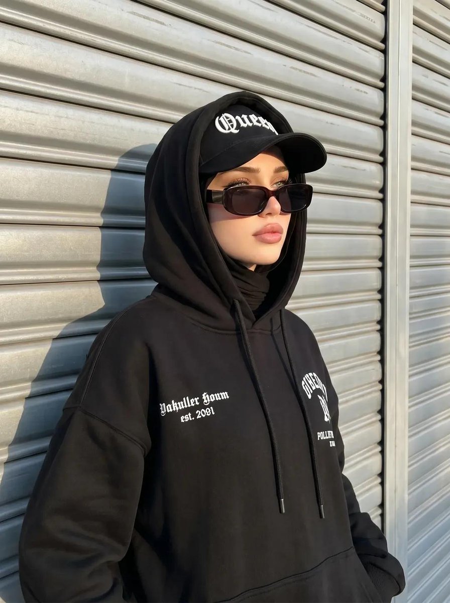创建一张与所附参考图片具有完全相同面部特征和特征的图像，不改变任何特征。 一张街头风格的头巾女性肖像，她有着冷酷前卫的气质。她戴着黑色头巾，一件胸前印有白色文字的超大黑色连帽卫衣…
