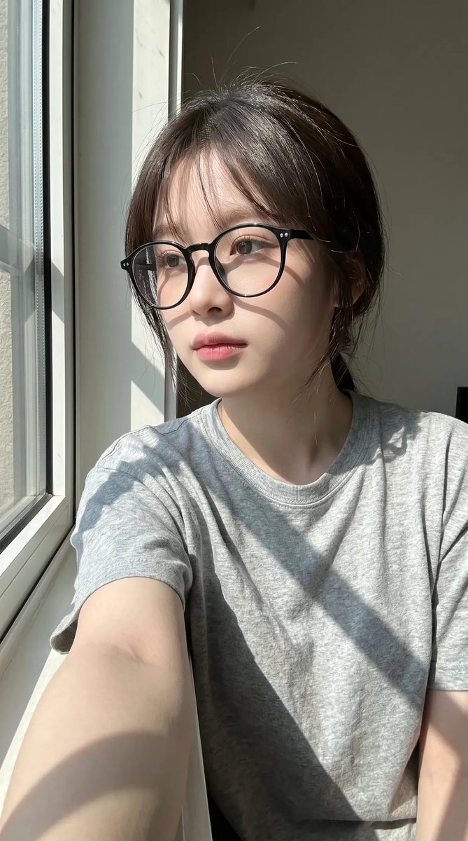 超写实抓拍式智能手机自拍照肖像：一位年轻东亚女性室内坐在一扇大窗户旁，处于明亮的自然日光下。保持与上传的面部参考高度相似的面部特征：柔和的椭圆形脸型、纤细的下颌线、自然偏窄的鼻梁…