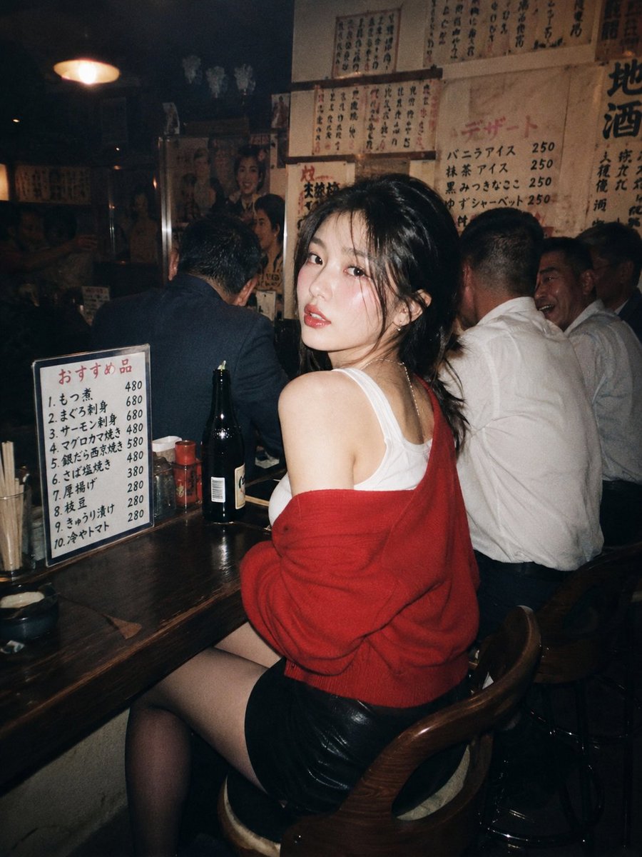 一位美丽的年轻东亚女性，留着深色波浪长卷发，妆容精致，夜晚坐在一家温馨昏暗的日本居酒屋的木质吧台前。她转过头，越过肩膀直视镜头，眼神妩媚诱人。她身穿白色背心，外搭一件红色针织毛衣…