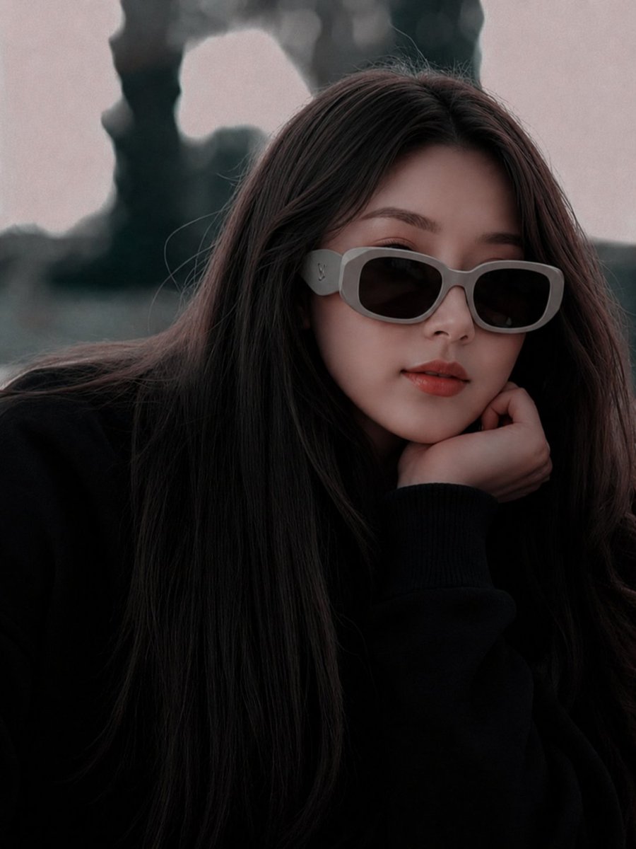 超现实电影级时尚人像:一位美丽的年轻东亚女性,长直深棕色头发,身穿超大黑色毛衣,佩戴厚重的哑光灰色奢侈品牌设计师太阳镜。她将下巴轻搁于手上,神情平静地望向镜头,拥有柔和自然的唇色…