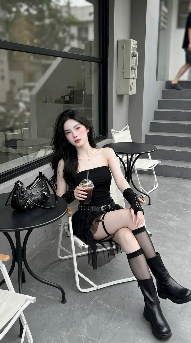 户外极简风格咖啡馆中，一位年轻女性的全身照片：长直黑发，坐在白色折叠椅上，身穿黑色抹胸迷你连衣裙、镶钉宽腰带、黑色无指系带护臂、大腿吊袜带、透明黑色及膝长袜、…