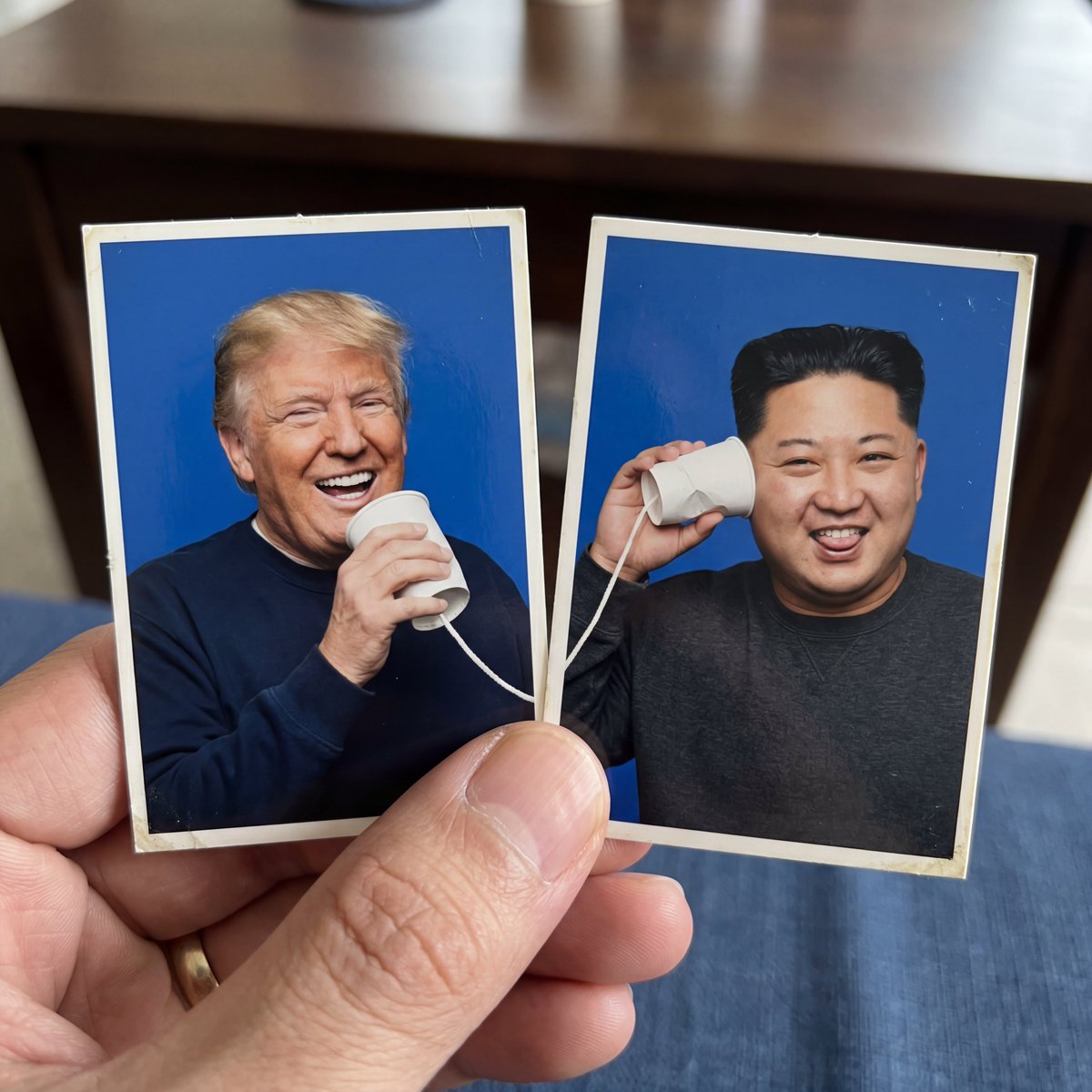 创作一个创意1:1正方形构图，包含两张并排摆放的护照式照片打印件，被一只手的拇指和食指捏住。使用上传的参考图像作为两个拍摄对象，准确保留每个对象的面部特征、发…