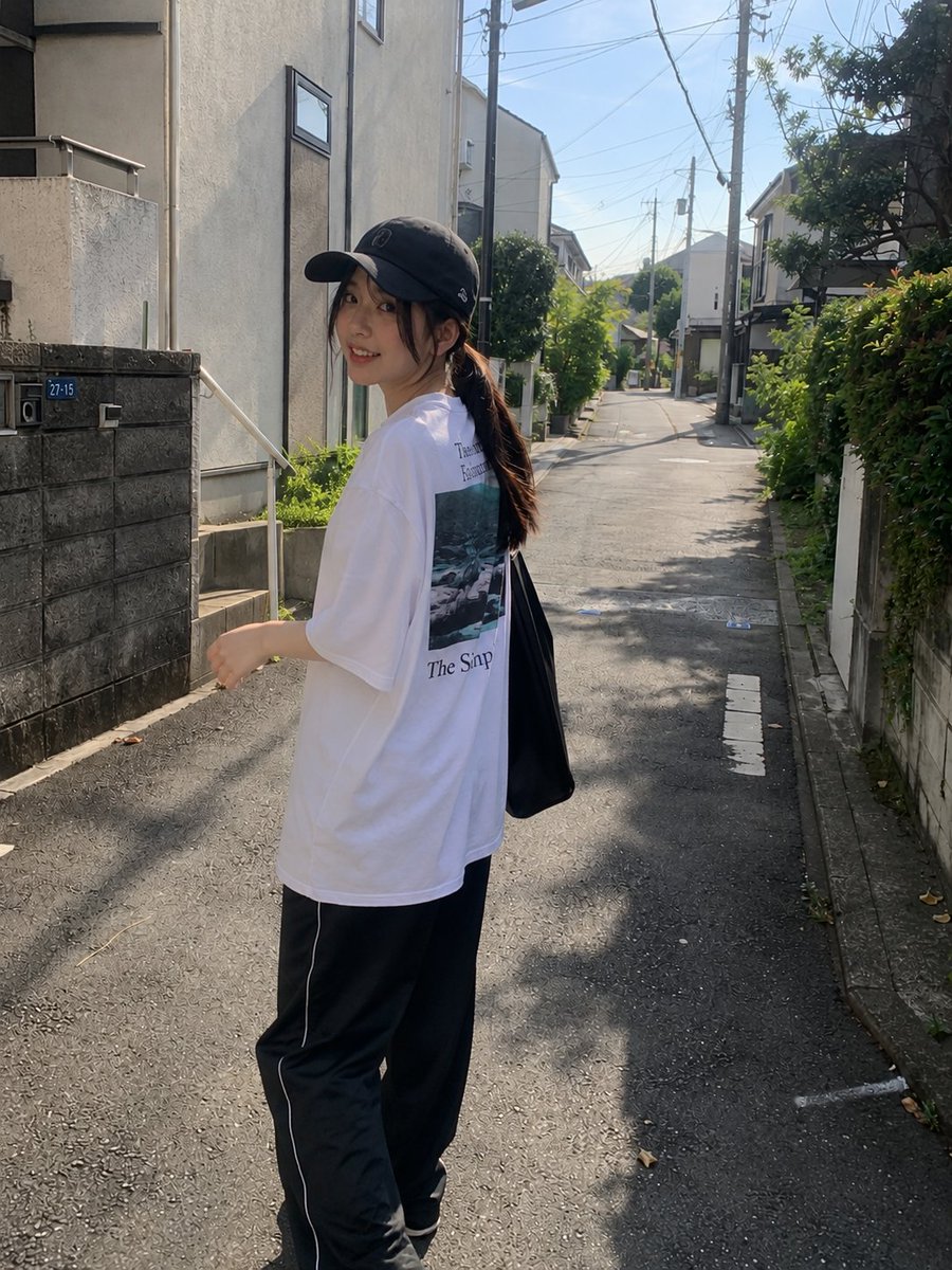年轻漂亮的日本女孩,肤色白皙,妆容自然柔和,长长的深色头发在黑色棒球帽下扎成低马尾,身穿宽松的白色印花T恤和黑色宽松全长运动裤。在一个晴朗的下午,她随意地走过一条安静的住宅小巷…