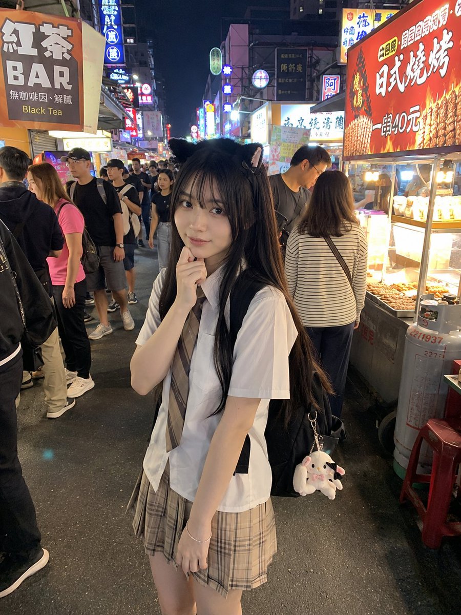 年轻的日本女孩，留着顺直黑色长发和柔软的刘海，戴着可爱的黑色猫耳发箍，身穿白色短袖衬衫、条纹领带和米色格纹百褶裙。她站在一个充满活力的亚洲夜市里，四周是霓虹招牌、美食摊位和熙熙攘…