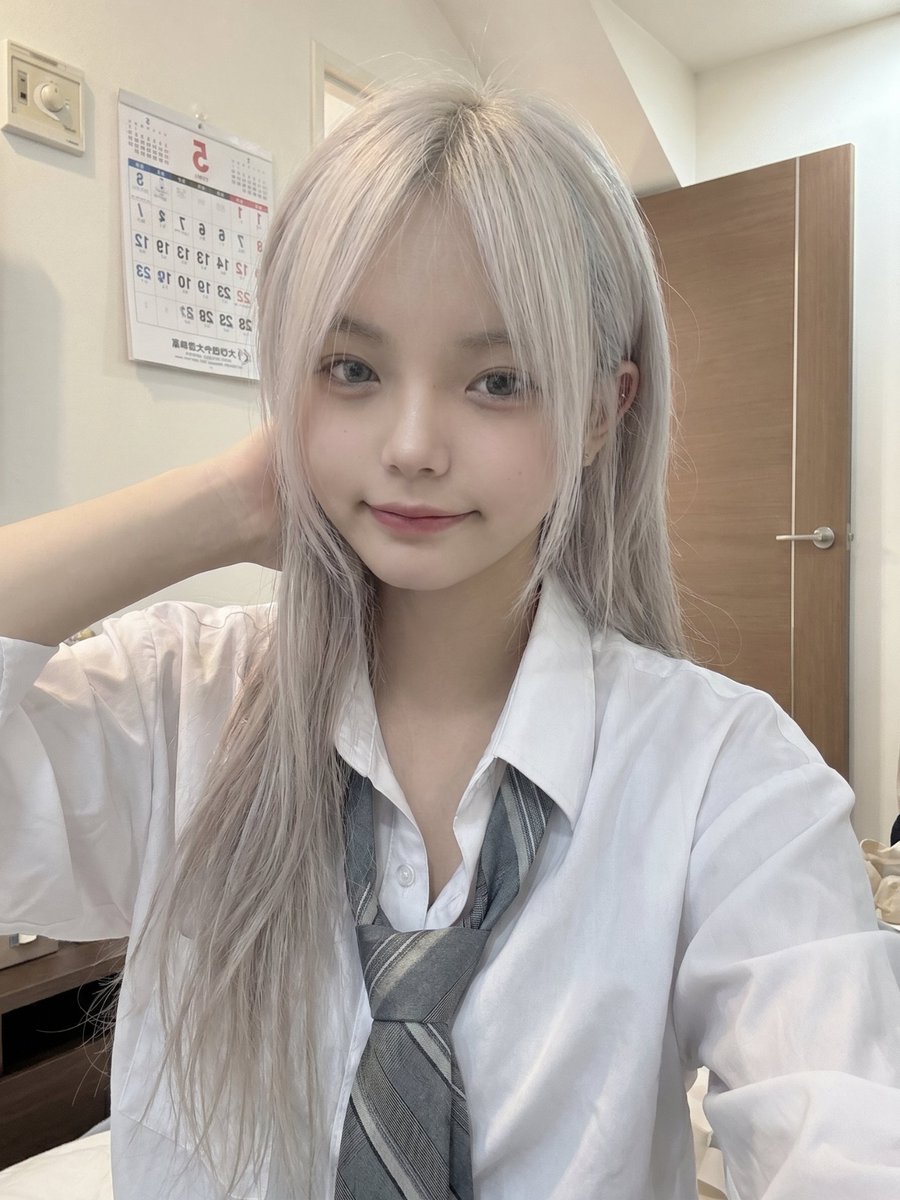 一位年轻的日本女孩,留着长长的银白色头发,柔软凌乱的刘海部分遮住眼睛,侧面编着一条用粉色丝带扎住的小辫子,穿着白色纽扣校服衬衫、灰色领带和校服。她随意地坐在室内,一只手托着脸,用…