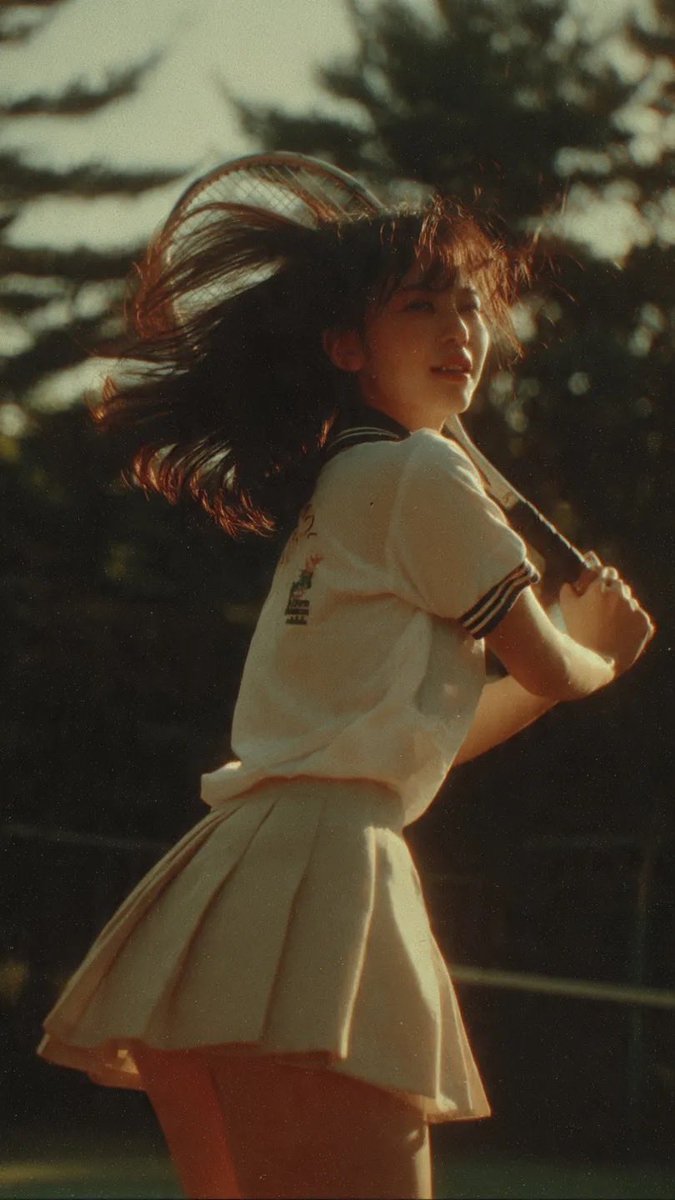 电影感中景镜头：一名身穿网球服的日本少女，在网球比赛挥拍途中被自然抓拍，柔和阳光穿过树林，暖色调，90年代日本电影美学，轻微胶片颗粒感，风吹动她的头发，动态而自然的动作，怀旧诗意…