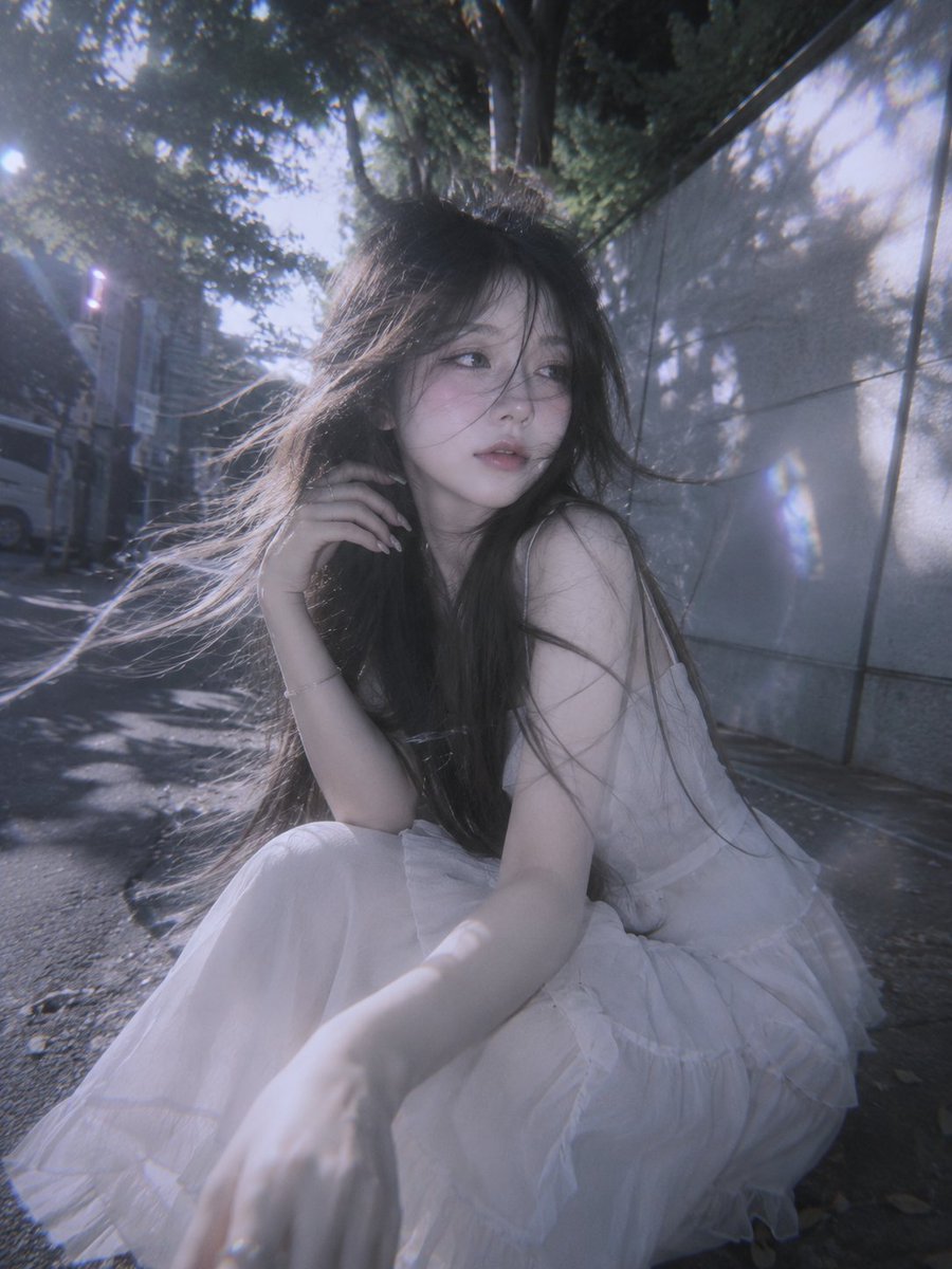 一位超现实的、如同人偶般的年轻女性，留着及腰的飘逸长发，以真实自然的抓拍肖像呈现，散发出柔和的日常魅力。她看起来有些害羞，但与镜头之间有一种温柔的联结，微风轻拂，发丝自然地在她脸…