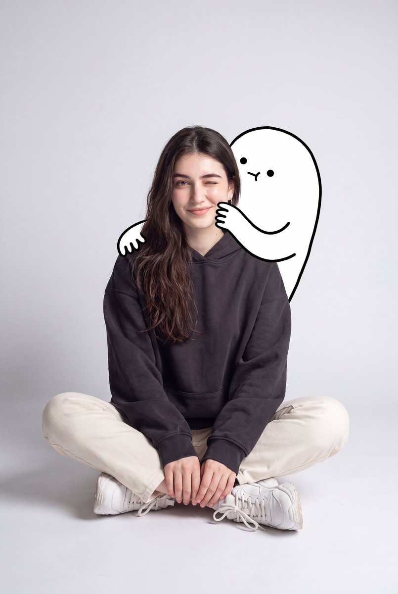 一幅可爱的极简风肖像：一位年轻女性随意地坐在地板上，身处一个光线柔和的灰色背景的简洁摄影棚中。她穿着一件宽松的深炭灰色连帽衫、奶白色直筒长裤、白色袜子和厚底白…