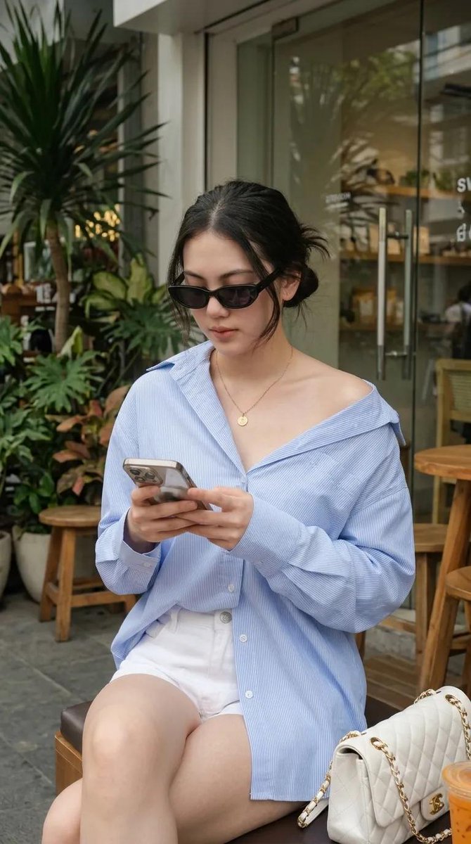 使用我的图片，生成一张 9:16 的图像 --- 一位年轻女性坐在户外咖啡馆，随性慵懒的 Oversized 风格。身穿宽松 Oversized 浅蓝色细条纹纽扣衬衫，袖子卷起…