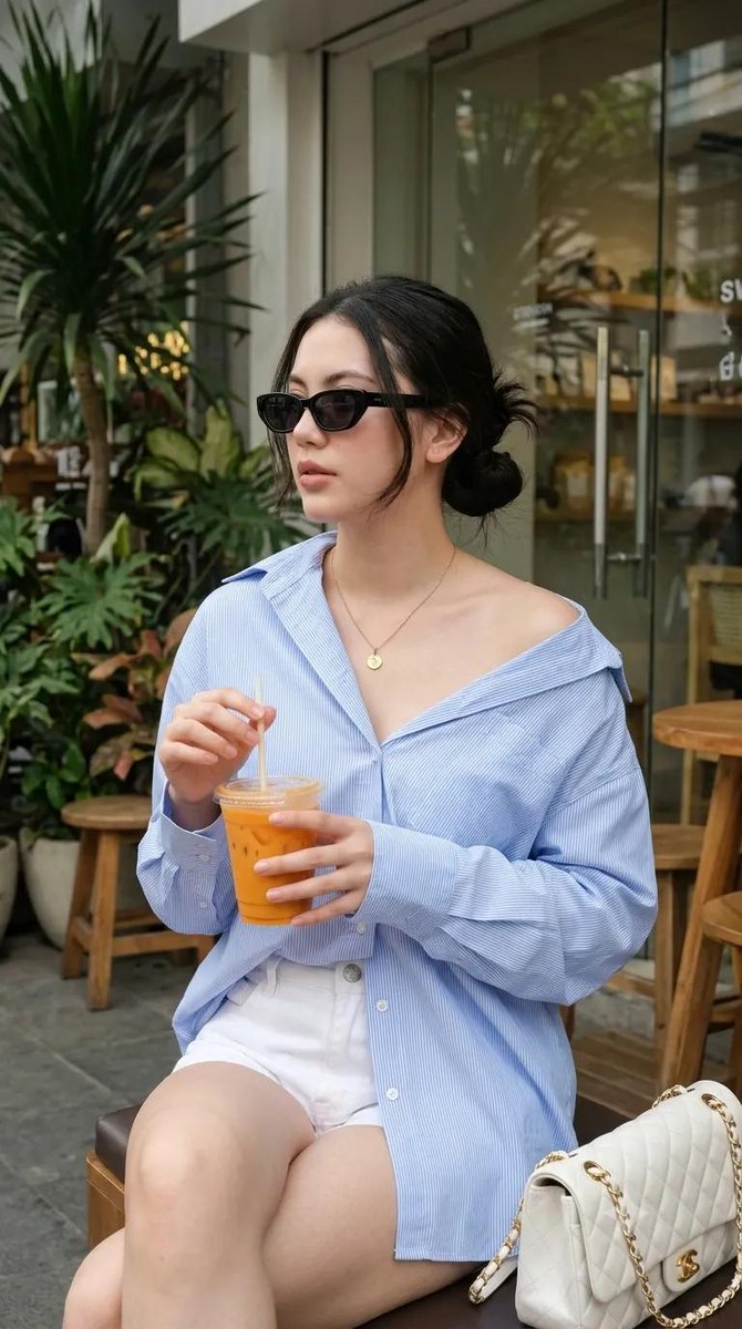 使用我的图片，生成一张 9:16 的图像 --- 一位年轻女性坐在户外咖啡馆，随性慵懒的 Oversized 风格。身穿宽松 Oversized 浅蓝色细条纹纽扣衬衫，袖子卷起…