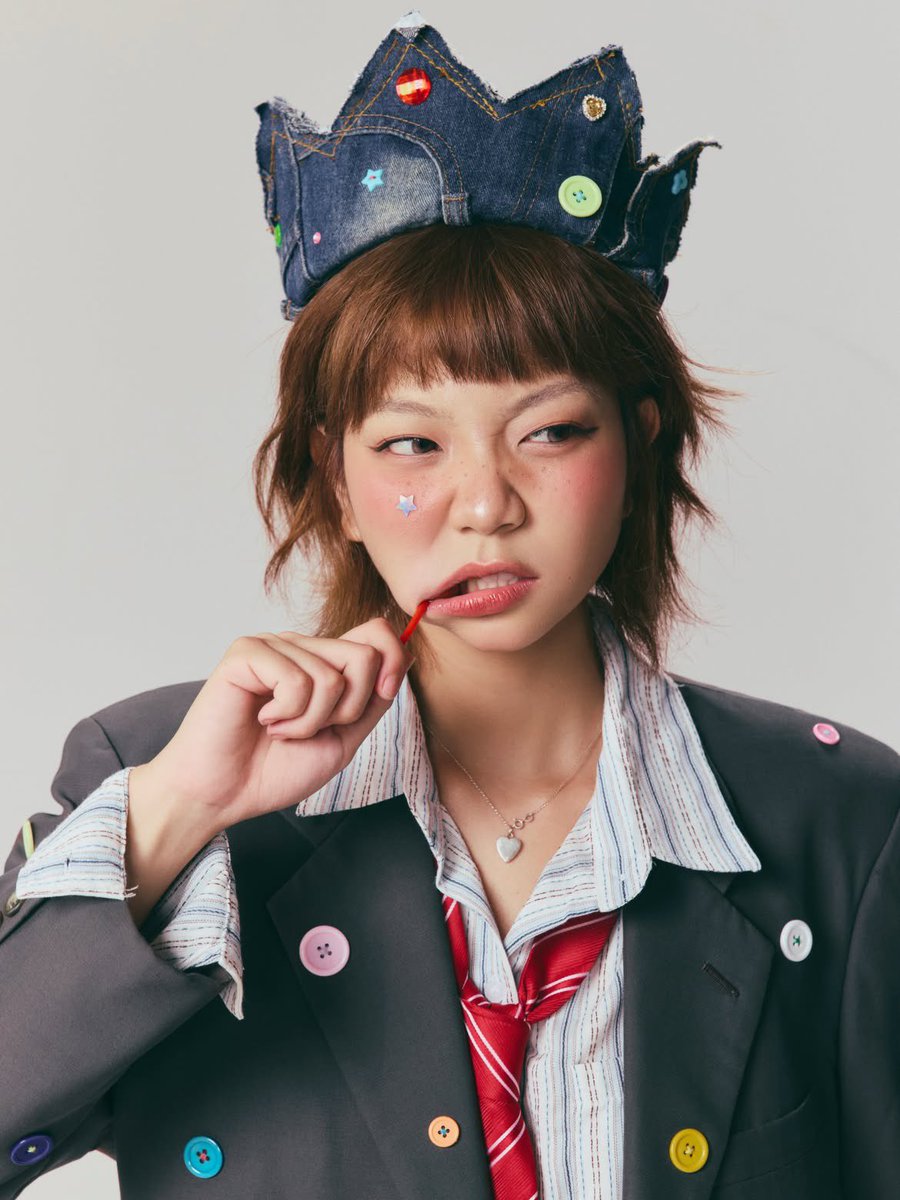 超写实编辑时尚肖像:一位俏皮的年轻女性,留着短款层叠栗棕色波波头与齐整的直刘海,柔和自然妆容配以玫瑰色腮红,鼻梁上有淡淡的雀斑,粉色光泽唇,长而卷翘的睫毛,搭配上挑眼线,一侧面颊…