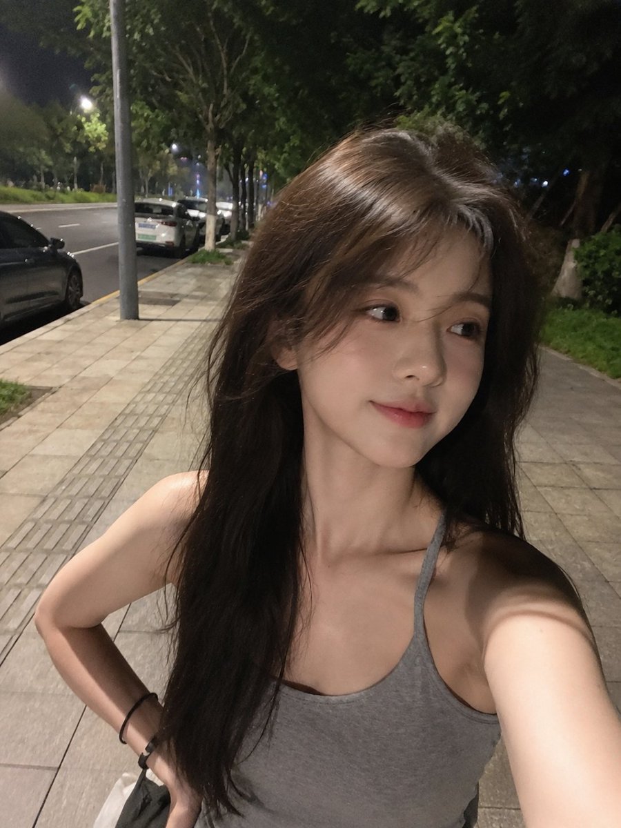 夜晚用手机拍摄的极致真实感智能手机自拍,看起来确实是用 iPhone/手机摄像头抓拍的,而不是单反相机。一位美丽的年轻东亚女性,留着浓密略带凌乱的深棕色长发,在微风中自然飘扬,拥…