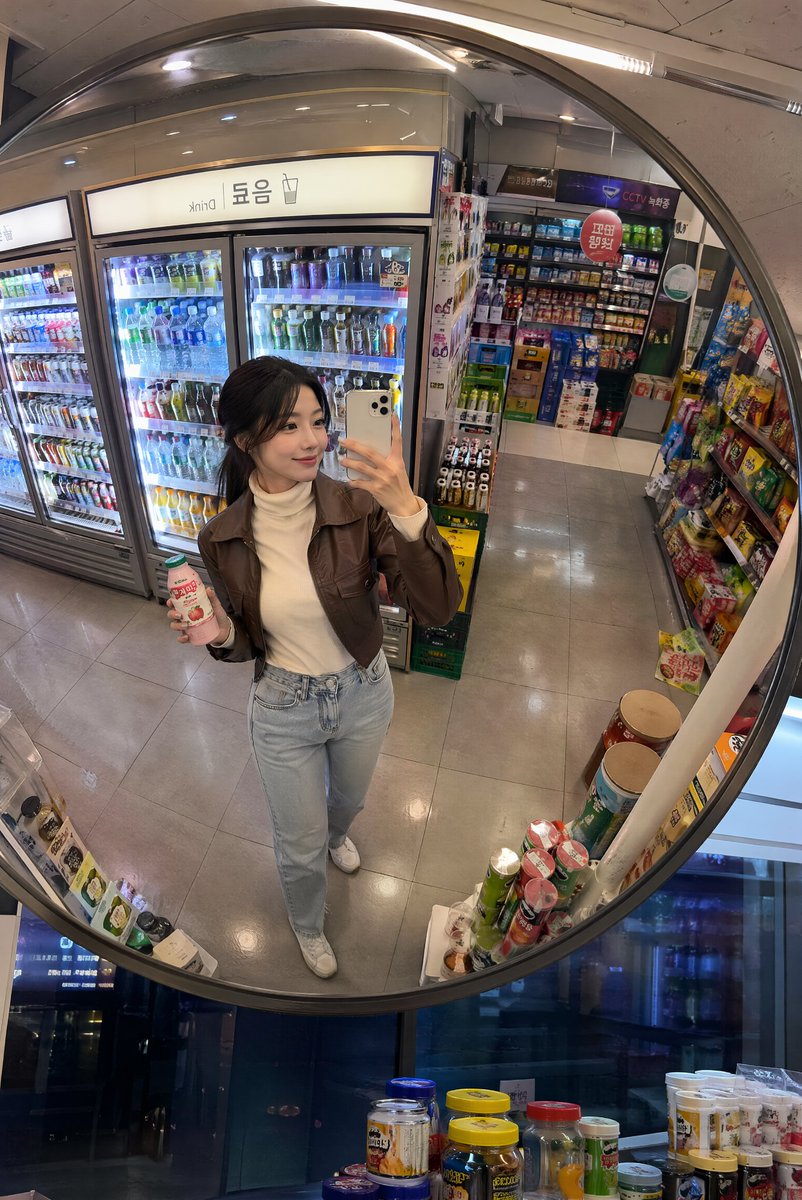 深夜韩国便利店镜面抓拍 创建一张逼真的生活方式照片，透过安装在韩国一家温馨便利店天花板上的一面大型凸面镜拍摄，场景为夜晚。画面中一位时尚的年轻韩国女性从略微抬高的镜面视角被捕捉到…