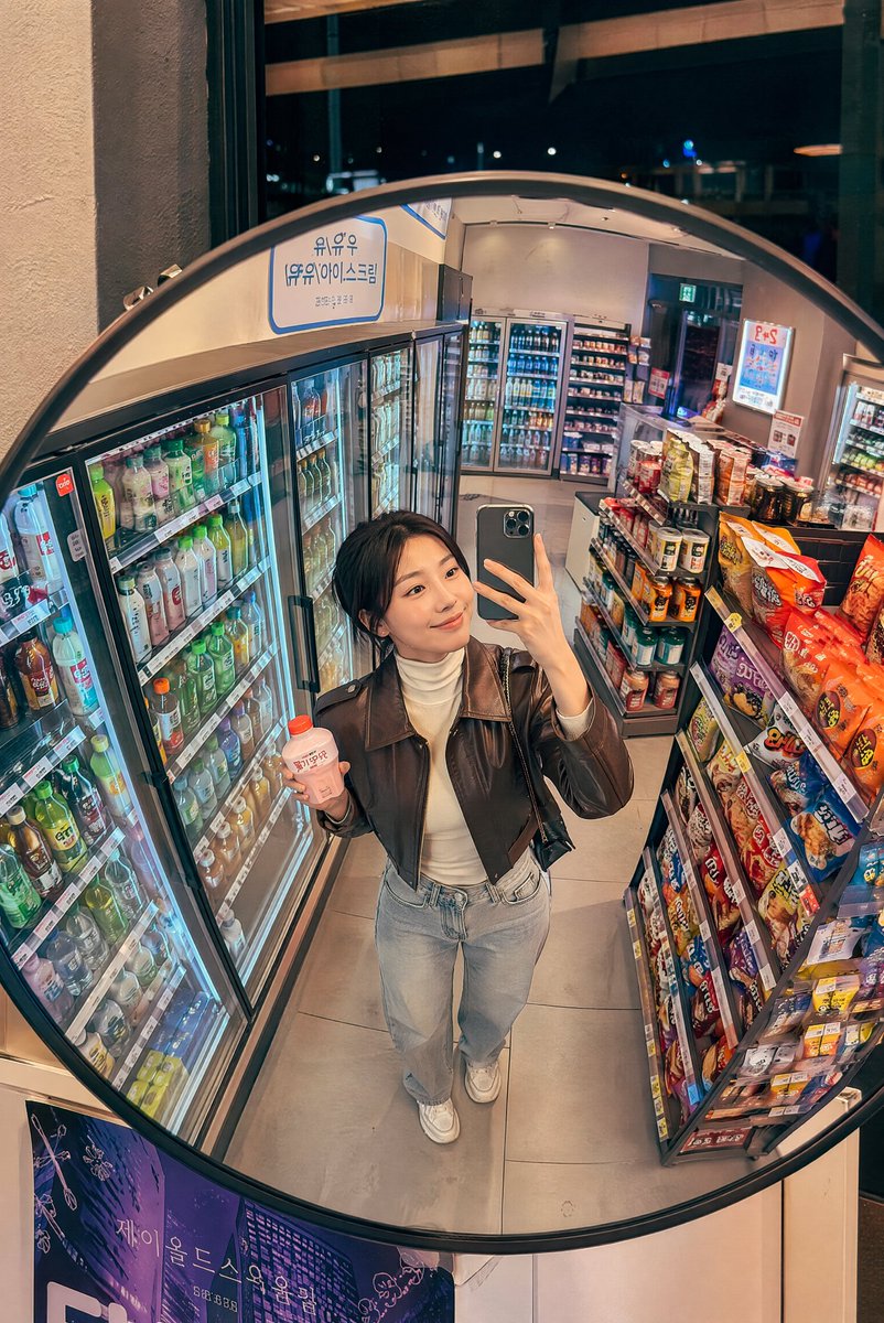 深夜韩国便利店镜面抓拍 创建一张逼真的生活方式照片，透过安装在韩国一家温馨便利店天花板上的一面大型凸面镜拍摄，场景为夜晚。画面中一位时尚的年轻韩国女性从略微抬高的镜面视角被捕捉到…