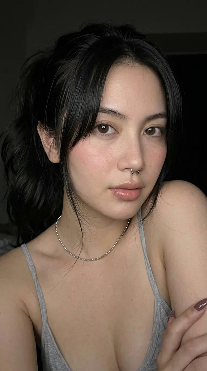 一张高端时尚工作室人像照，主体是一位年轻女性，肤色白皙，深棕色头发梳成光滑的高发髻。她呈紧凑的蹲姿，膝盖紧贴胸口。她平静、自信、神情平和地直视镜头。她身穿一件奶油色抹胸（心形领口…