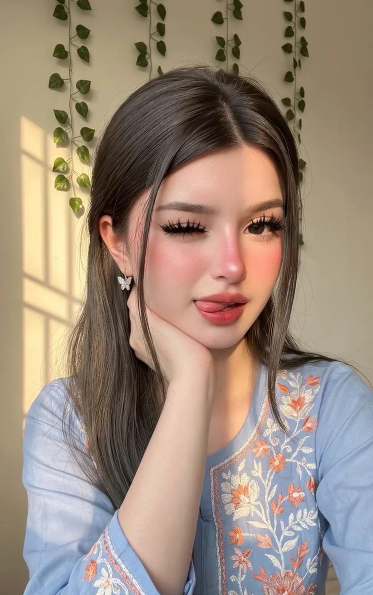 请原样保留她原有的面部特征。她天生容貌美丽，面部对称性完美。她应显得年轻且有女性魅力，拥有自然丰满的胸部，而非平坦的胸部。 这是一张室内特写自拍照，照片中是一位年轻女性，面容柔和…