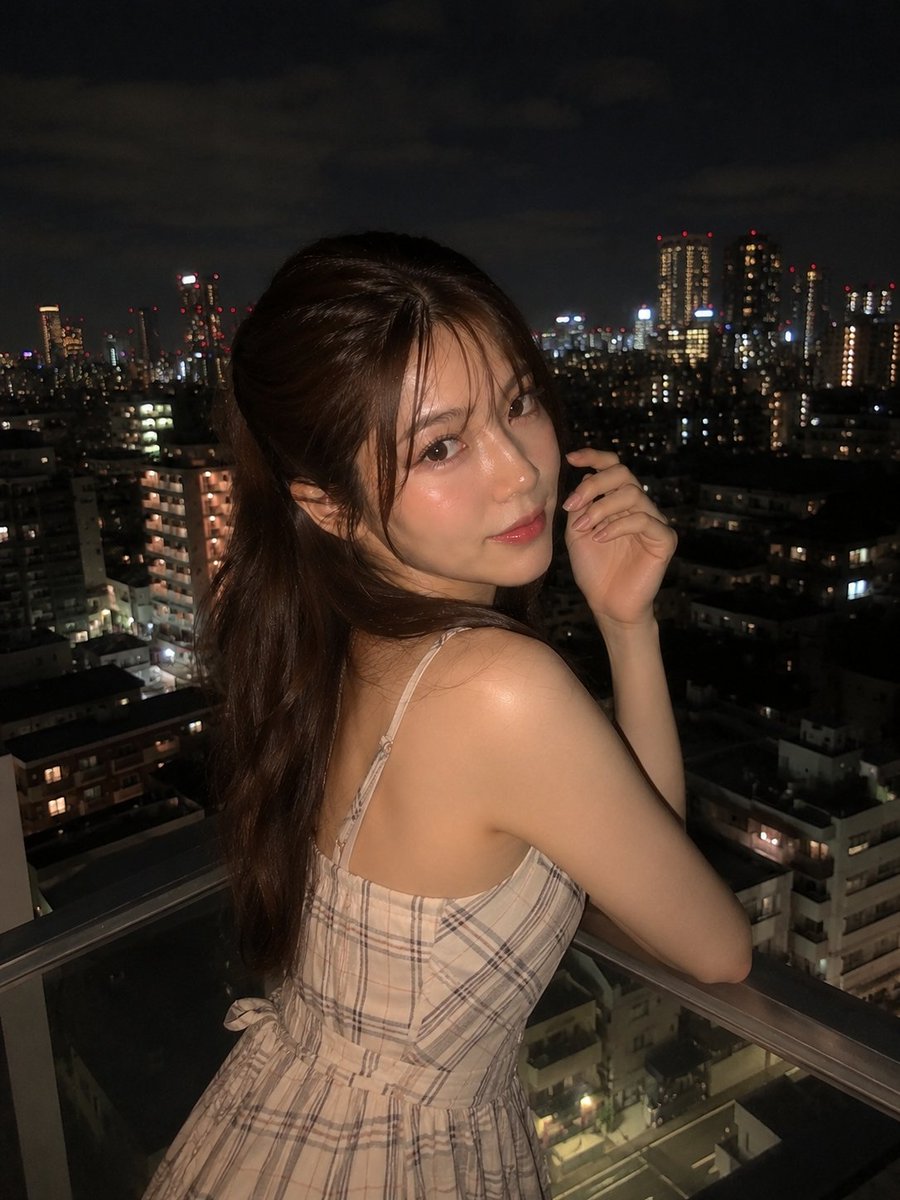 超写实夜景人像:一位美丽的年轻女子站在阳台上,俯瞰城市天际线,身穿优雅的无袖米色格纹连衣裙,淡雅腮红妆容,自然水润唇妆,慵懒的半扎发造型,几缕碎发自然垂落于脸颊两侧。她回眸望向镜…