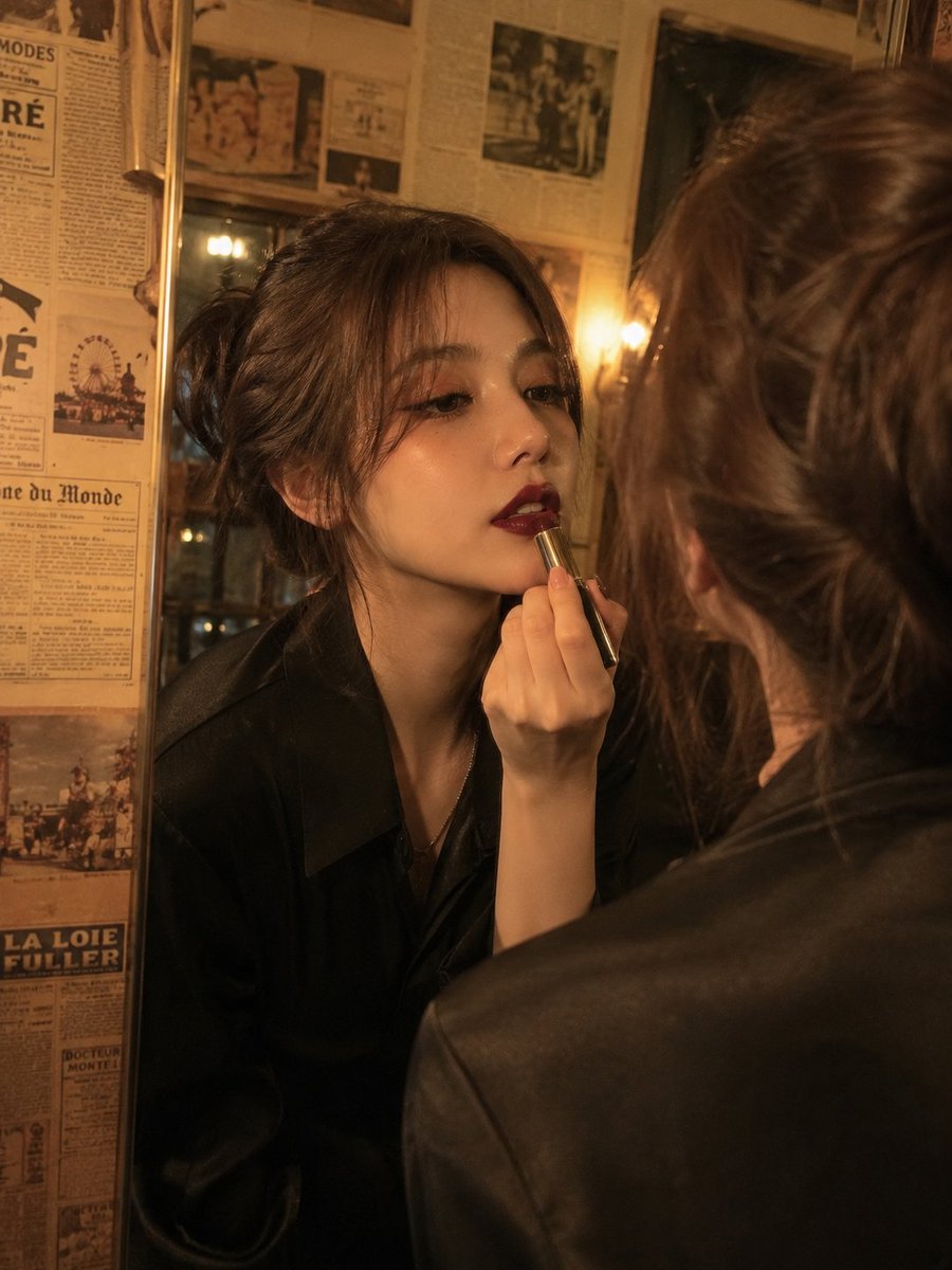 电影级复古美人肖像：一位优雅的年轻女性正在涂抹深酒红色口红，同时望向镜中，温暖的金色钨丝灯光在她脸上投下戏剧性的阴影，柔软的波浪棕色头发盘成略显凌乱的发髻，肌肤无瑕，妆容大胆，配…