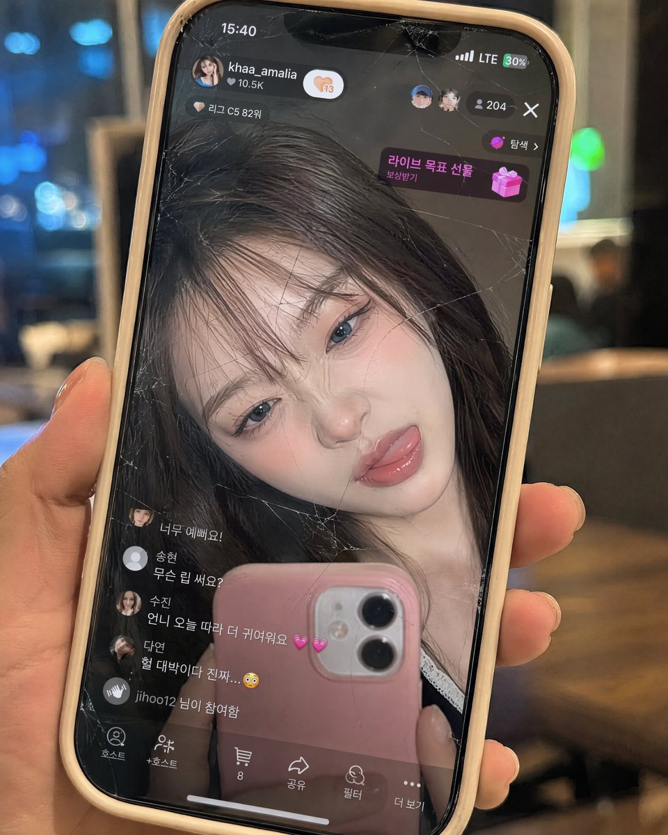 完全保留参考图片中韩国女性的面孔——不要改变她的脸型、眼睛、鼻子、嘴唇、比例、肤质或整体身份。制作一张超写实的9:16特写,画面中是一只从右侧伸出的右手握着的米色硅胶壳iPhon…