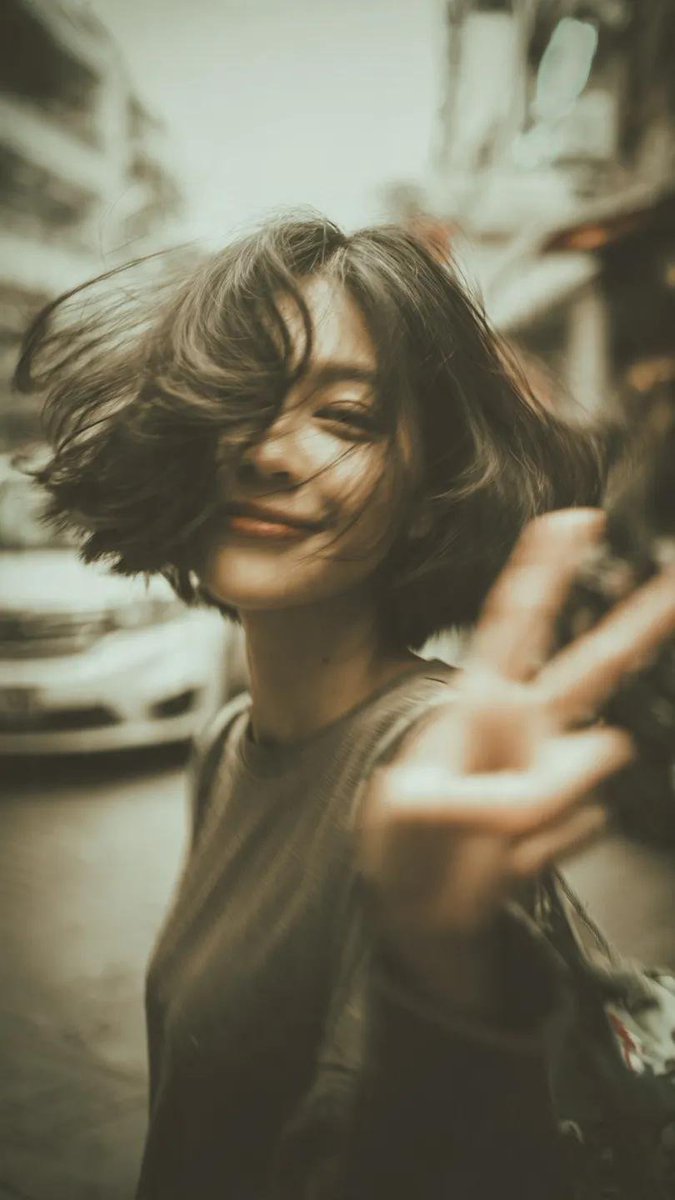 一张千禧年(Y2K)风格的街拍人像写真:一位开朗的年轻女性,留着凌乱的短波波头(bob),自然地开怀大笑,直接对着镜头比出胜利手势(V字手势/peace sign),她伸出的手占…