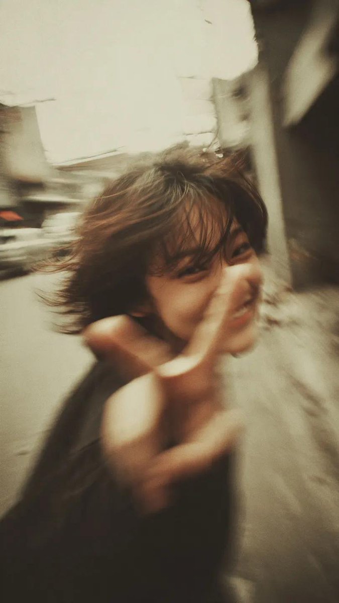 一张千禧年(Y2K)风格的街拍人像写真:一位开朗的年轻女性,留着凌乱的短波波头(bob),自然地开怀大笑,直接对着镜头比出胜利手势(V字手势/peace sign),她伸出的手占…