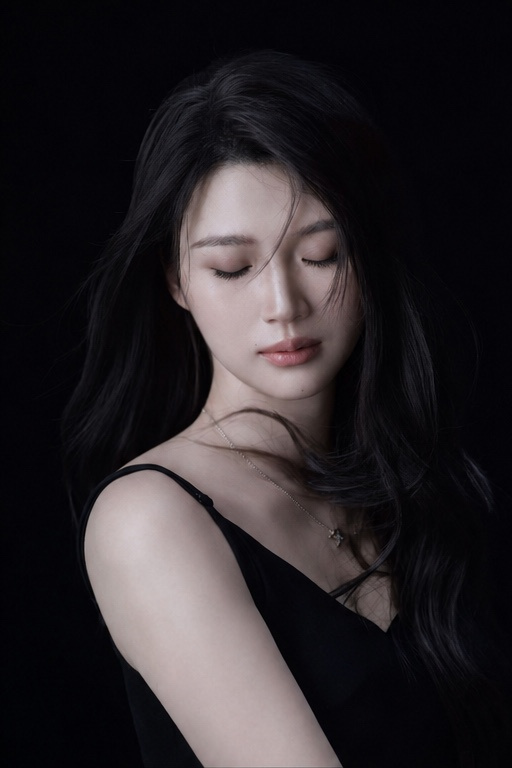 一位年轻成年东亚女性站在纯黑色摄影棚背景前,画面为近景到半身肖像,人物位于中央略偏右。身体以三分之二侧身朝向画面左侧,左肩更靠近镜头,头部轻轻回转看向镜头,形成安静自然的侧身回眸…