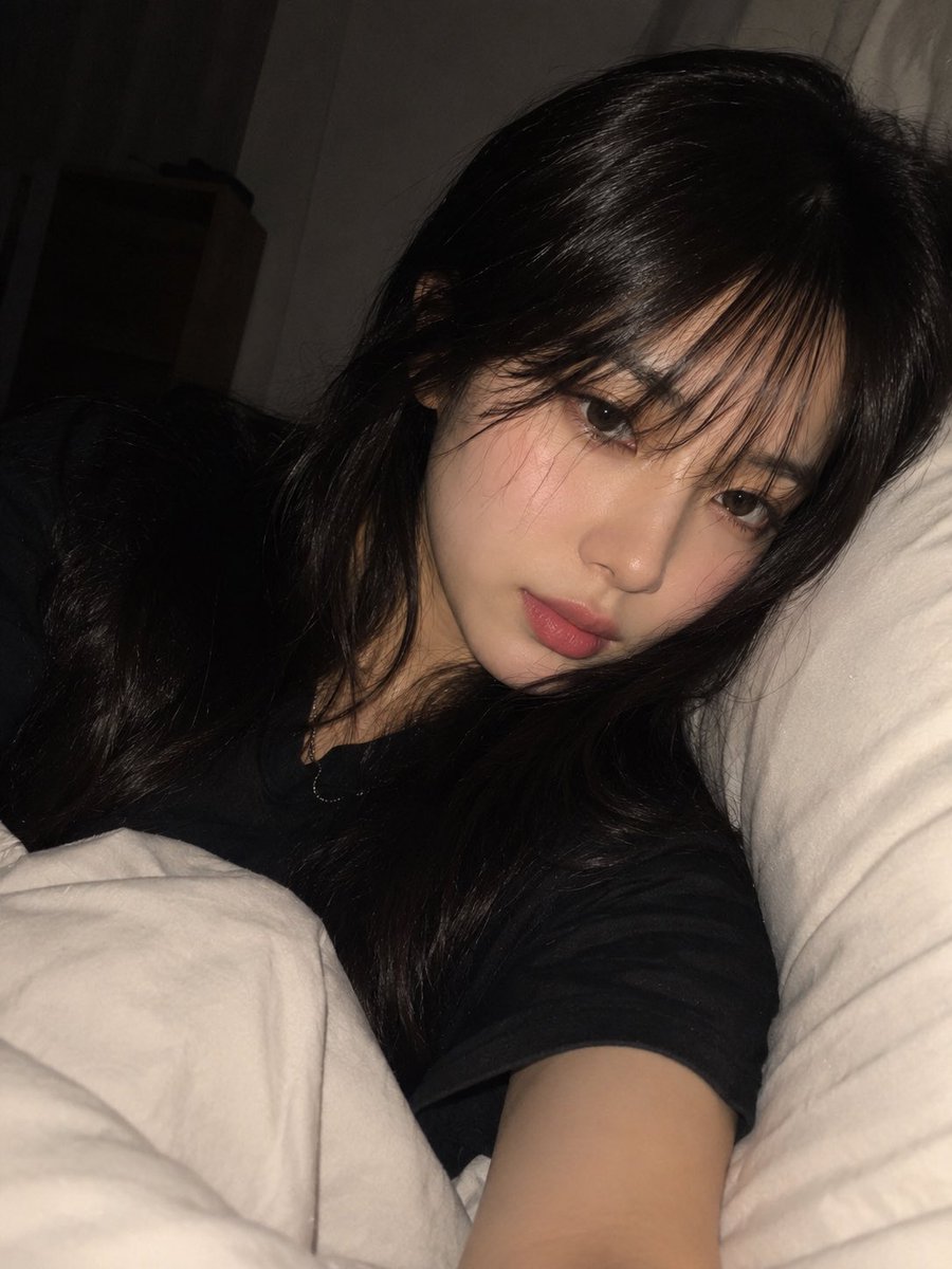 一张高度写实、亲密的夜间卧室自拍，照片中一位年轻成年东亚女性舒适地躺在床上，以一种随意、自发的智能手机拍摄方式捕捉，拍摄于即将入睡的时刻。请使用上传的图片作为…
