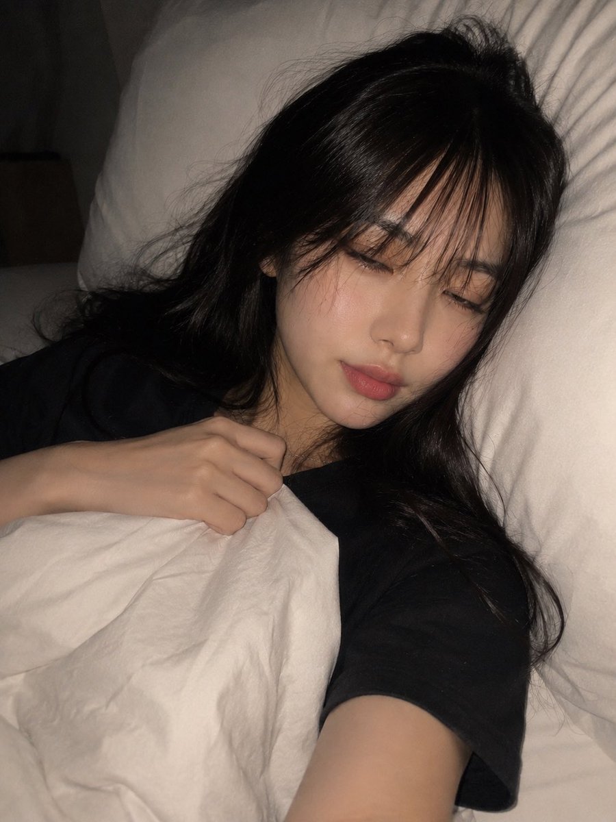 一张高度写实、亲密的夜间卧室自拍，照片中一位年轻成年东亚女性舒适地躺在床上，以一种随意、自发的智能手机拍摄方式捕捉，拍摄于即将入睡的时刻。请使用上传的图片作为面部和外貌参考，保持…