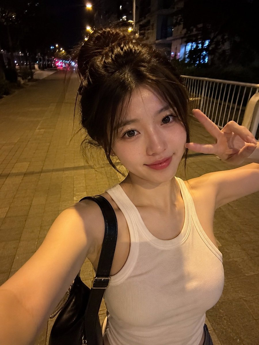 夜晚,一位美丽的东亚年轻女性在安静的城市人行道上户外行走的真实感智能手机自拍。她拥有瓷白肤色、闪亮的大眼睛呈深棕色、小巧笔挺的鼻梁、自然有光泽的粉嫩双唇,以及精致年轻的面部特征…