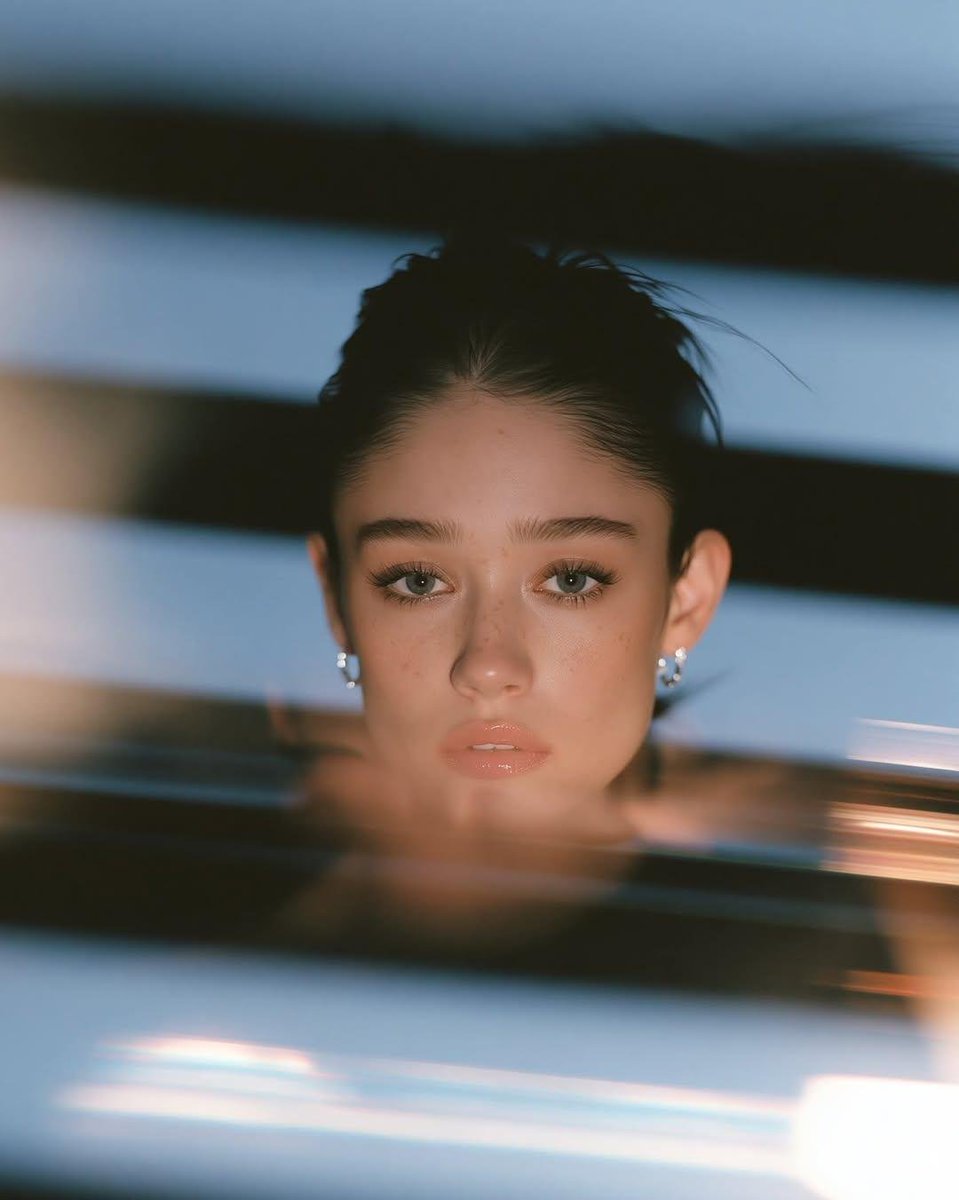 超写实电影感特写肖像:一位美丽的年轻女子,光滑的深色头发梳成整洁的低发髻,浓密的自然眉毛,淡淡的雀斑,裸色亮泽唇彩,带有逼真毛孔的无瑕肌肤,佩戴小巧的银色圈形耳环,身着极简黑色服…