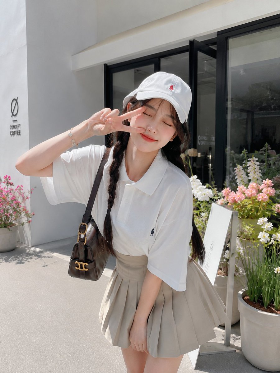 一张迷人的、照片写实风格的生活方式人像照:一位美丽的年轻日本女性,在晴朗的阳光下,于一家现代极简风格的咖啡馆外俏皮地摆姿势。她微微前倾,在脸旁俏皮地比出可爱的剪刀手,闭着眼睛露出…