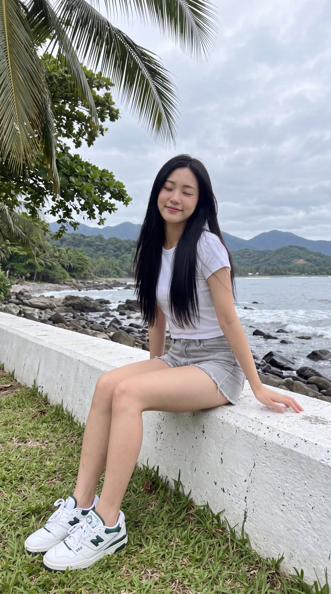 [Nano Banana Prompt] 一张写实风格的照片：一位年轻的东亚女性，长长的直发顺滑乌黑，披散在肩背两侧，随意坐在一道低矮的白色混凝土海堤上。她身穿一件素色白色短袖T…