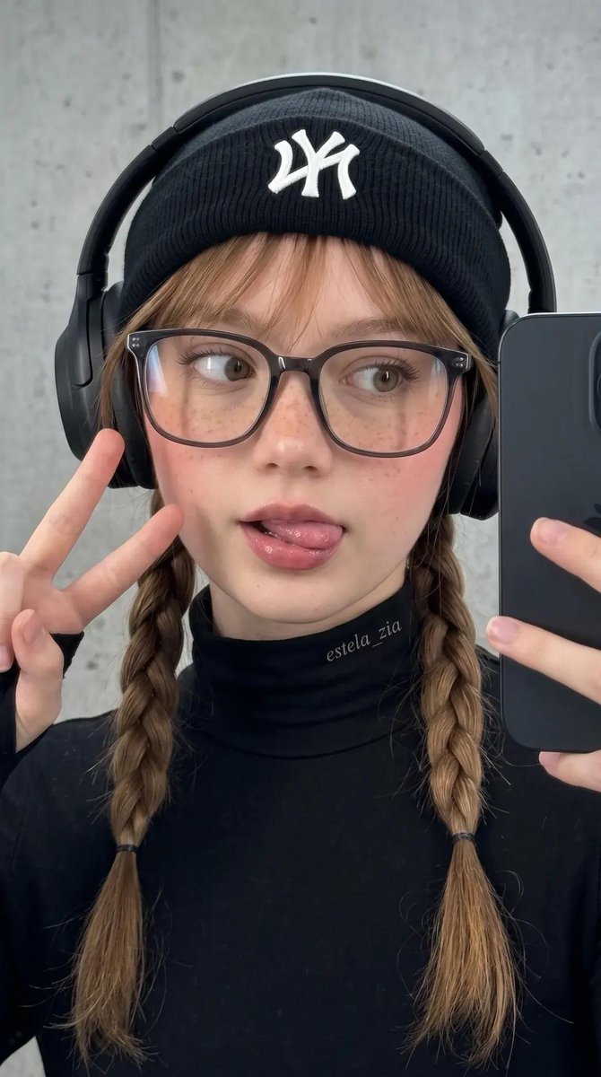 不要改变她的脸部。一张酷感都市街头风的时尚年轻女性特写自拍肖像。她身穿全黑装束,搭配修身高领上衣、带白色logo的黑色毛线帽、夸张的黑色头戴式耳机,以及大框透明黑框眼镜。她的头发…