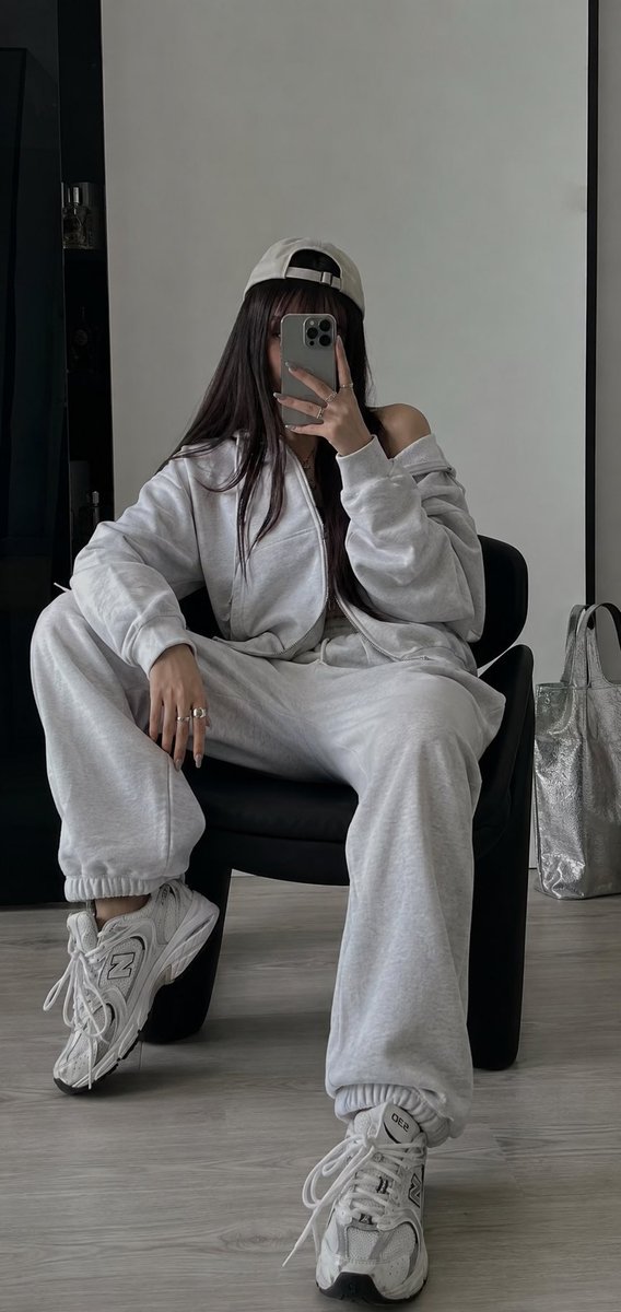 以我上传的照片作为面部参考。 使用 iPhone 拍摄。 在一个极简、明亮的房间里拍摄的一张摆拍镜子自拍照。一名年轻女子随意地坐在一把低矮的黑色椅子上,双腿舒适地分开,身体微微后…