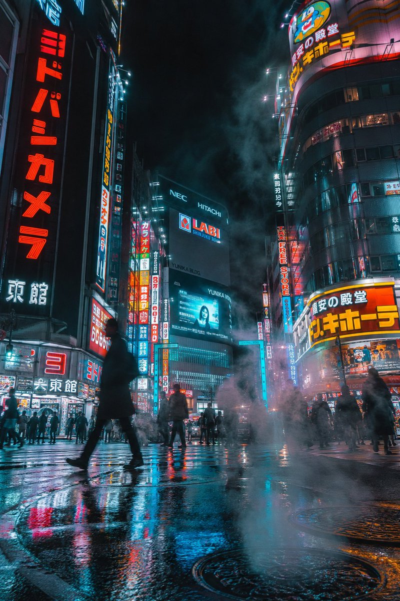 夜晚的未来赛博朋克城市街道，竖向构图。霓虹招牌（包含清晰的日文文字）在高耸的摩天大楼上发光。湿润的人行道倒映着鲜艳的灯光与全息广告。浓重的蒸汽从下水道井盖升起，融入霓虹照亮的雾气…