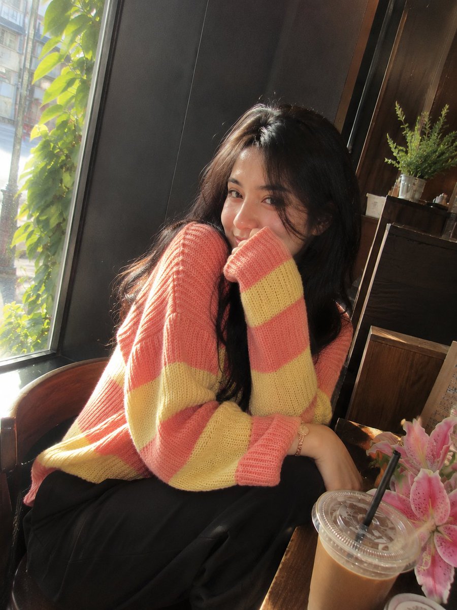照片级写实风格的影院感咖啡馆肖像:一位美丽的成年女性,留着长而自然卷曲的深棕黑色头发,皮肤柔和泛光,五官精致,眼神富有表现力。她身穿宽松舒适的针织毛衣,交替呈现柔和的粉色与浅黄色…