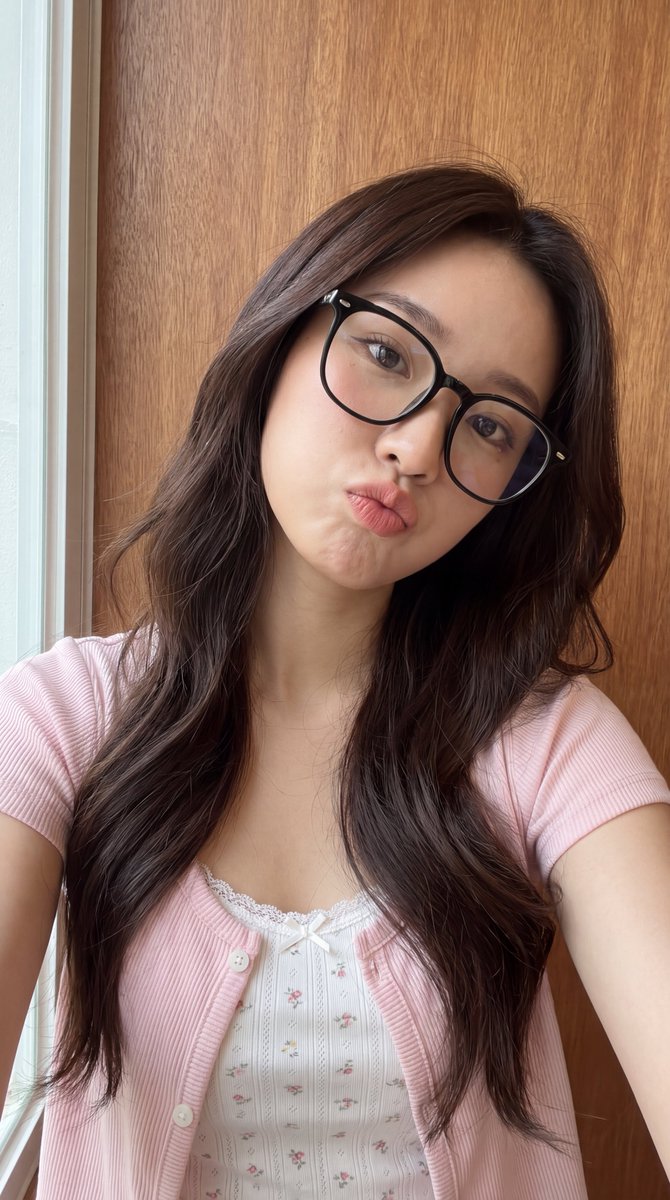 [Higgsfield 营销工作室图像提示] ar 9:16 4K High 一位年轻东亚女性的近距离自拍肖像，长长的波浪状深棕色头发垂落在一边肩膀上。她戴着一副大号黑框眼镜，俏…